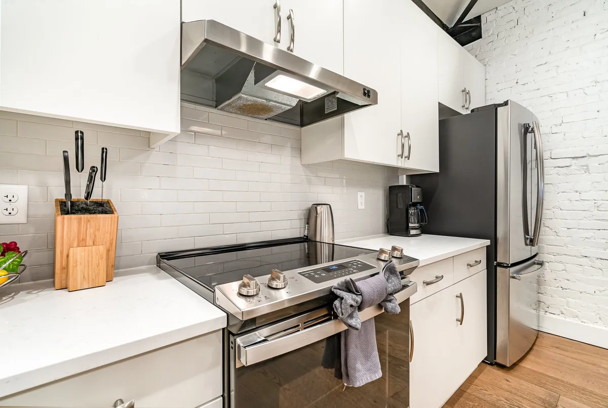 A stylish, modern kitchen centered around a stainless steel stove, modern cabinetry, and a kitchen island with a pristine countertop. Utensils are neatly displayed, highlighting both practical and aesthetic elements for meal prep and socializing.