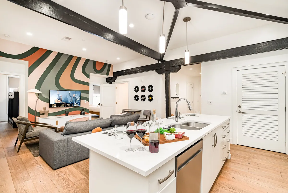 This image captures a spacious open-concept living area anchored by a large sectional sofa, vibrant wall art, a kitchen island with drinks, and an entertainment area with a prominent TV. The stylish yet comfortable setup is designed for both relaxation and group entertainment, perfectly reflecting the 'social hub' atmosphere.