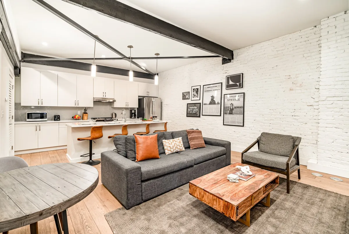 A contemporary living area with a comfortable sofa, kitchen area, coffee table, and modern wall art. The space is designed for relaxation and socializing, offering flexible seating for groups.