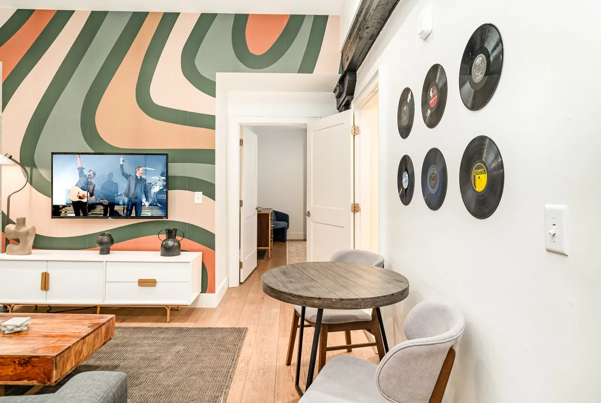 A creative and lively living space with colorful wall art, a TV set up for entertainment, stylish furniture, and a vinyl record display. The energy of the room is playful and welcoming, with obvious accommodations for both entertainment and relaxation.