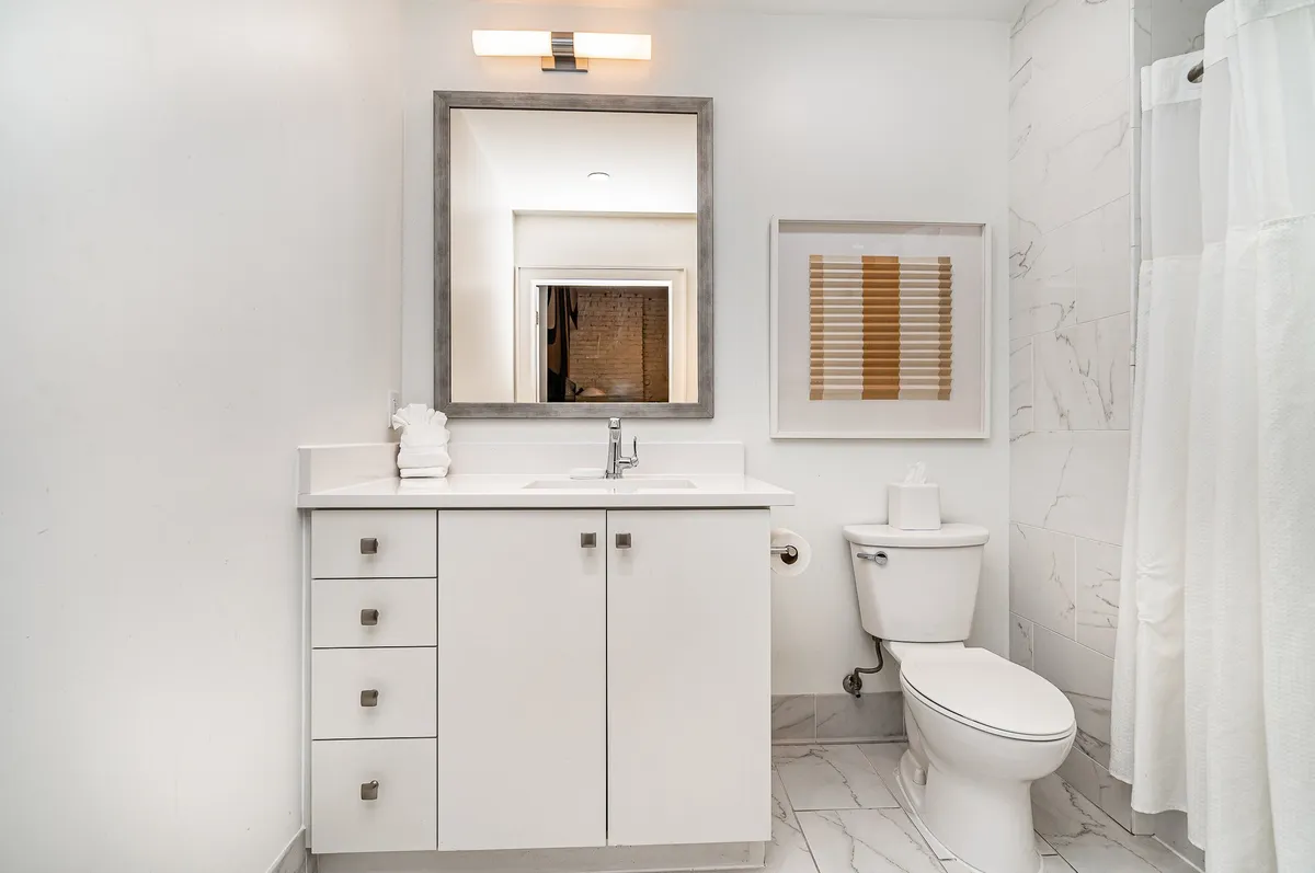 This image features a bright, modern bathroom with a large mirror, sleek sink, and a well-designed shower area. The space exudes a sense of calm and cleanliness, with soft lighting and neutral tones that suggest comfort and relaxation.