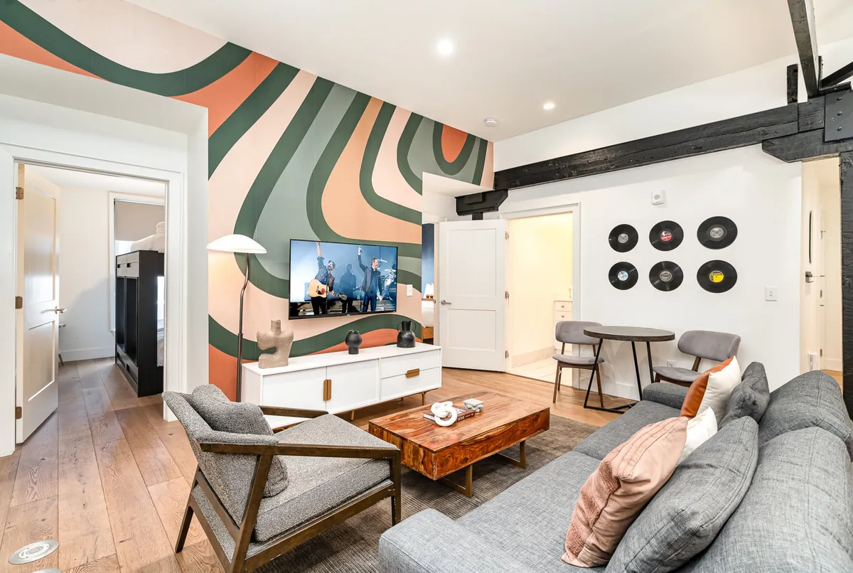 The hero image features a stylish living room with a vibrant, colorful accent wall, modern furnishings, and a wall adorned with unique record-themed art. A comfortable seating area is centered around a sleek coffee table and large television, inviting guests to relax and socialize in a cozy, contemporary space.