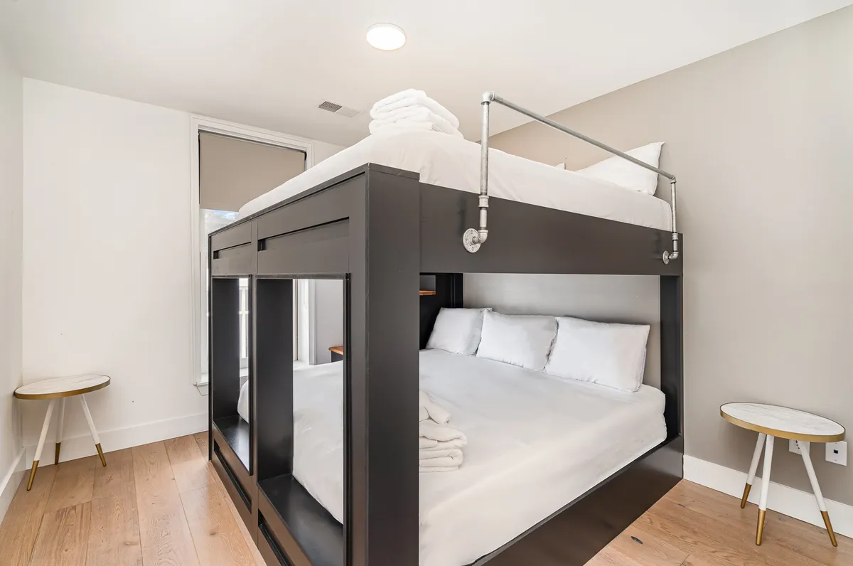 A cozy bunk bedroom with a white bunk bed, inviting white linens, and small side tables. The arrangement is ideal for groups, evoking a sense of fun and camaraderie typical of a memorable sleepover.