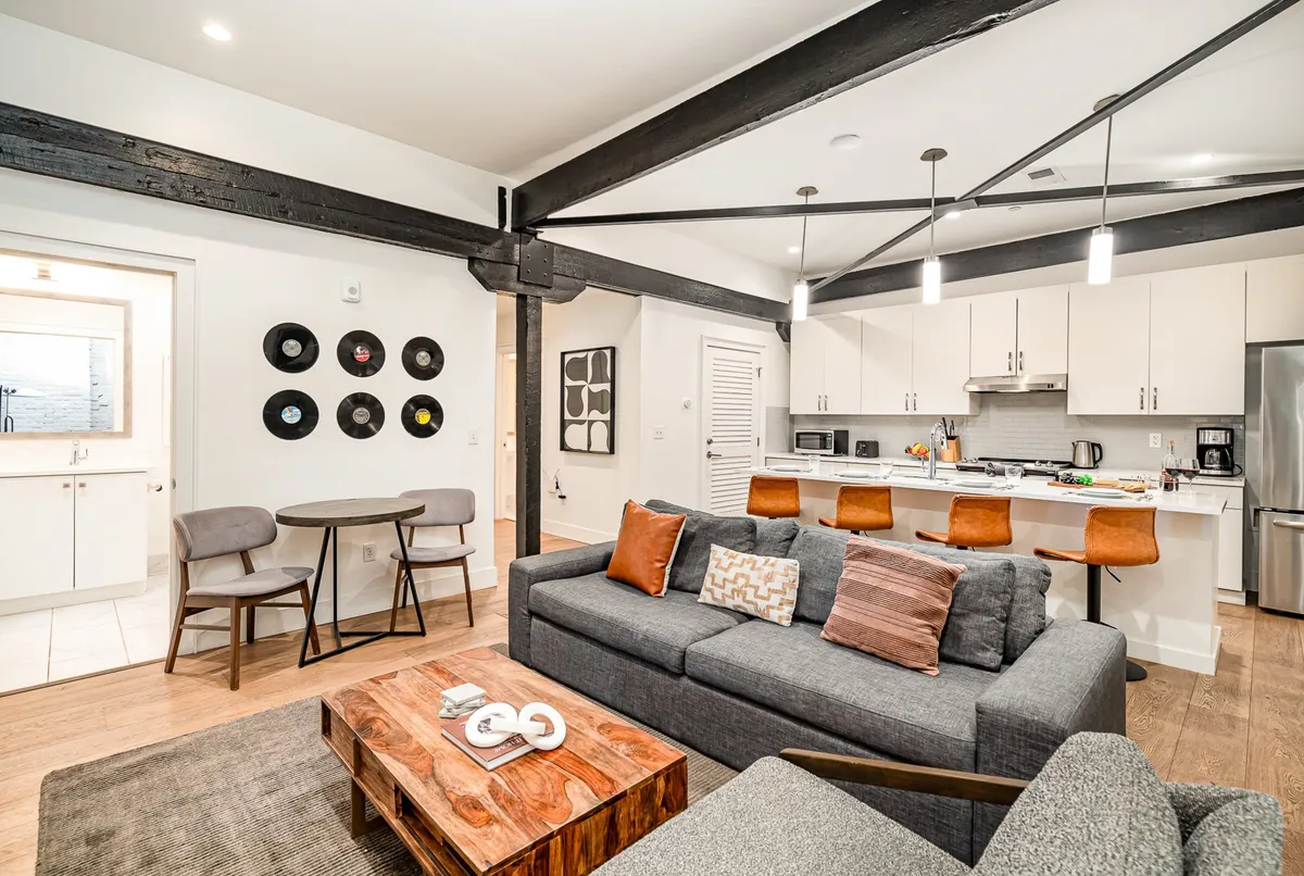 A cozy, contemporary interior featuring a comfortable sofa, a versatile coffee table, visible kitchen area, and wall art with vinyl records, suggesting musical inspiration. The open flow between spaces and intimate decor highlight opportunities for relaxation, music, and social activities.