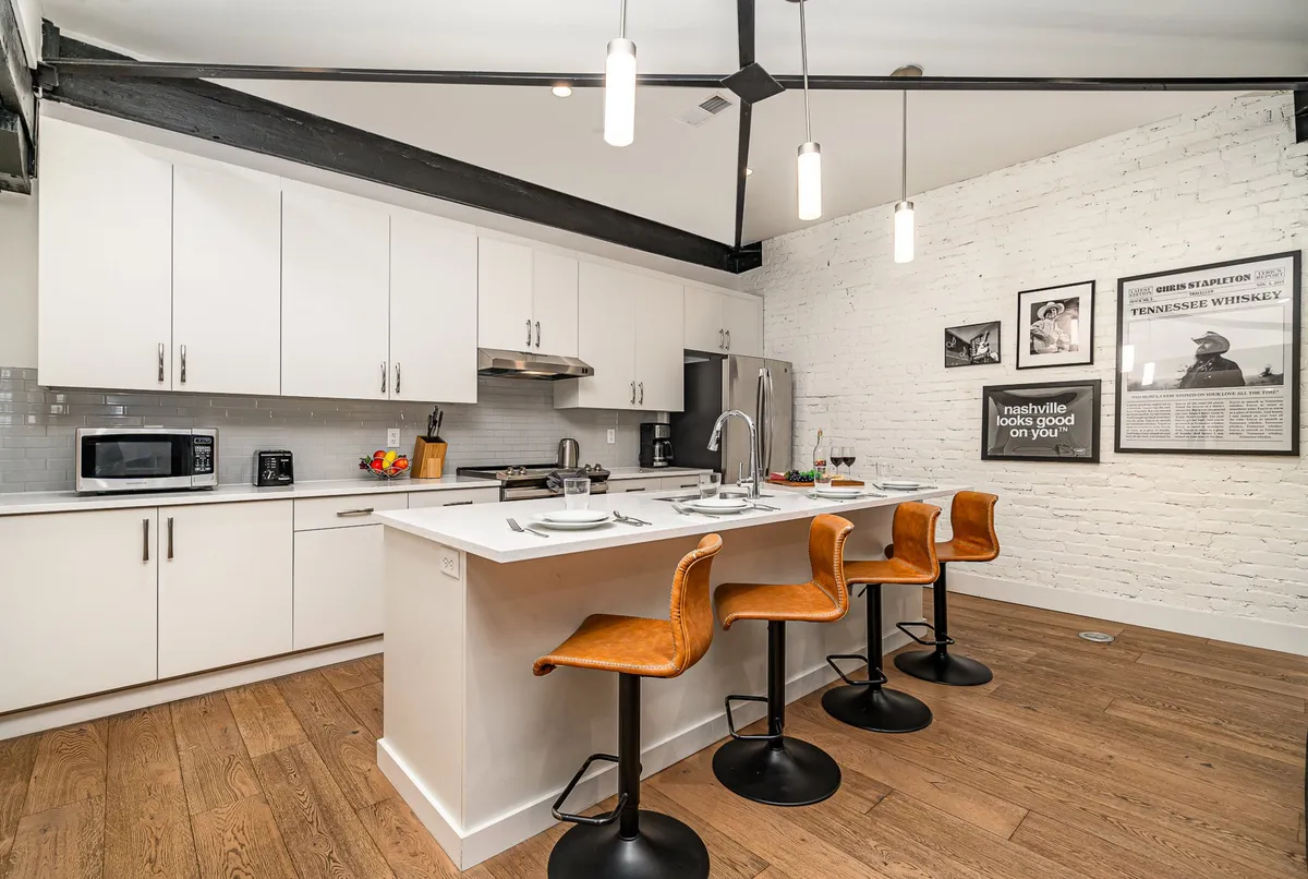 A kitchen interior focusing on white cabinetry, an inviting kitchen island, and industrial-style bar stools, with decorative wall art adding a homey touch. The space suggests casual dining and moments of togetherness.